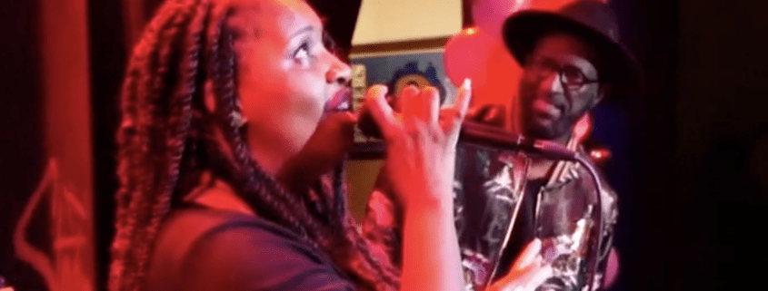 Woman singing passionately on stage, musician watching.